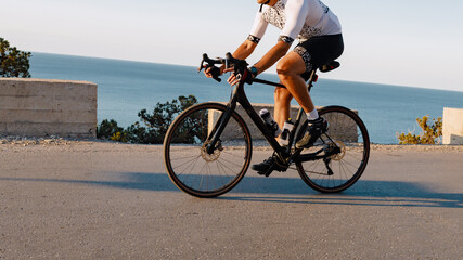 Naklejka premium Cyclist rides along coastal road during sunset in warm weather near the ocean