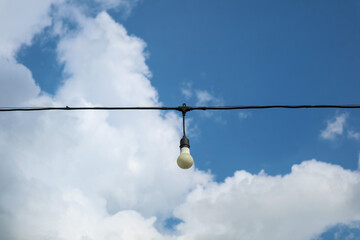 Obraz premium String of five decorative light bulbs hanging from a black wire against a cloudy sky, creating a moody outdoor ambiance with contrast between artificial lighting and natural weather backdrop