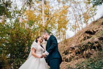 Fototapeta premium Portrait of beautiful bride and an elegant groom in nature, surrounded by a forest.