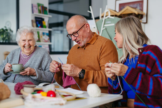 Group of senior people learning knitting together with caregiver tutor in a community center.