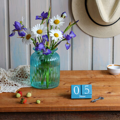 Rustic wooden table with turquoise vase of irises and daisies, vintage June 5 calendar, ripe and unripe strawberries, old key and straw hat for cozy country charm