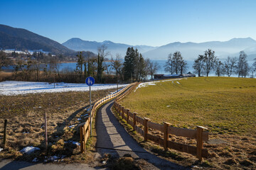 Fototapeta premium Idyllic walking trail along Lake Tegernsee in Upper Bavaria. The trail runs directly along the shore and offers a sweeping view across the lake to the surrounding mountains.