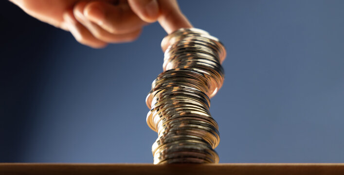 Hands supporting unstable coin stack symbolizing financial risk, market uncertainty