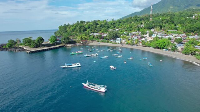 Cinematic drone orbit showing traditional outrigger boats anchored in a calm bay near a lush tropical village in Flores, East Nusa Tenggara.