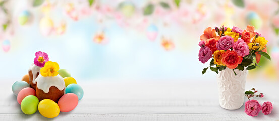 Festive Easter scene with colorful eggs, traditional cake, and a vibrant flower bouquet on a white wooden table.
