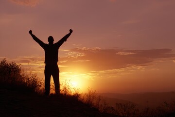 Fototapeta premium An inspiring silhouette of a person raising arms in victory or praise, bathed in the warm glow of a beautiful sunset.