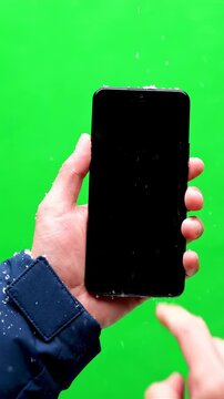 Person Holding Black Smartphone With Snow Falling Green Screen Background Blue Jacket Detail
