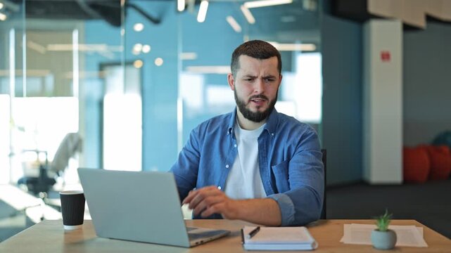 Professional working on laptop appears frustrated by loud office distractions, covering ears in distress. Seeking quiet amid busy environment. Feelings of annoyance and discomfort visible.