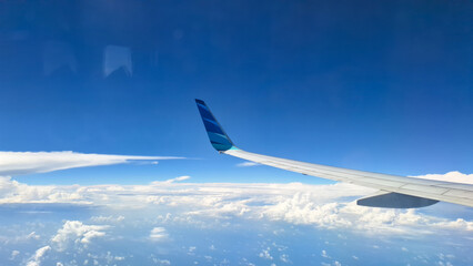 Fototapeta premium Airplane wing flying above clouds under a bright blue sky
