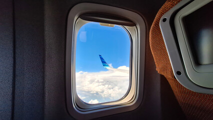 Fototapeta premium Airplane window view showing wingtip above clouds under a bright blue sky