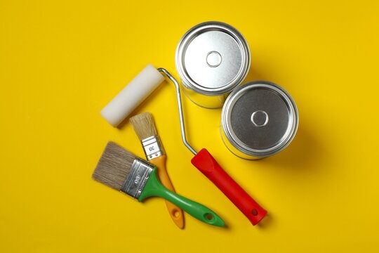 Brushes and paint cans on yellow background. Top view, copy space. Appartment renovation, repair, building and home design concept
