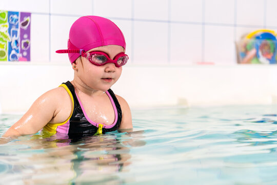 Child with pink swimming cap and goggles in pool.