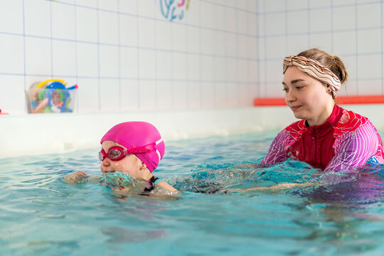 Young child learning to swim with a woman coach in a pool.