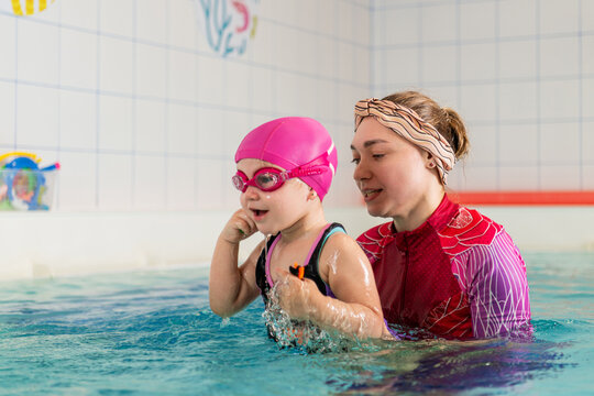 Young child learning to swim with a woman coach in a pool.
