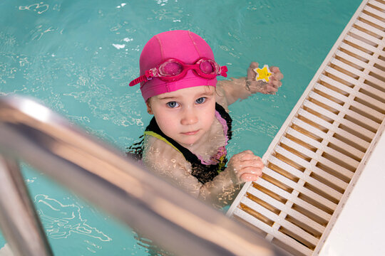 Cute little girl with pink swimming cap and goggles in pool