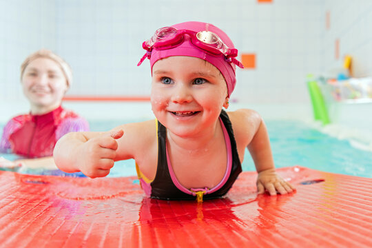 child learning to swim in pool with pink swim cap and goggles.