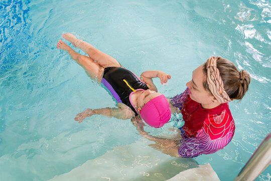 Woman swimming instructor teaching child to float on back in pool.