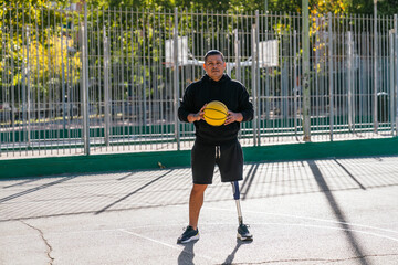 Obraz premium Male basketball player with a prosthetic leg holding a yellow basketball on an outdoor court, symbolizing sports, determination, and inclusivity