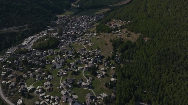 Aerial drone footage of the town of Saas-Fee with views over Allalin, Saas-Allmagell and Saas-Grund on a clear bluebird autumn day. Green valley floor contrasts with snow-covered alpine peaks.