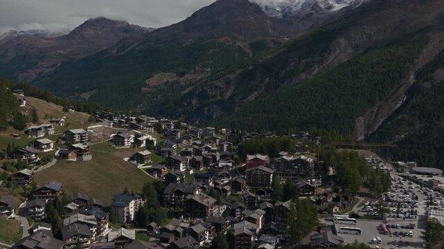 Aerial drone footage of the town of Saas-Fee with views over Allalin, Saas-Allmagell and Saas-Grund on a clear bluebird autumn day. Green valley floor contrasts with snow-covered alpine peaks.