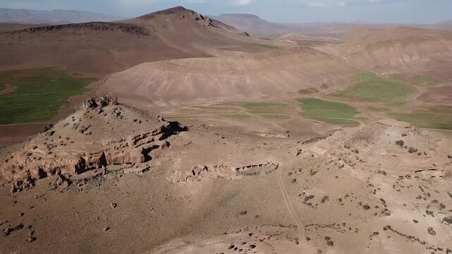 Aerial drone shot of a unique mountain peak in the High Atlas. Features natural geological caves used as ancient human storage shelters and a rock fortress in the Moroccan wilderness.