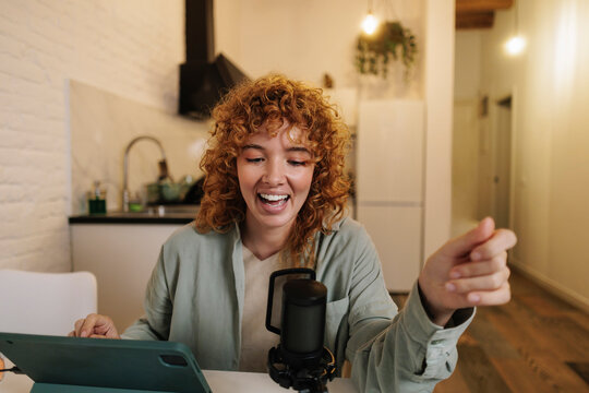 Smiling woman doing live broadcast using tablet PC and microphone at home