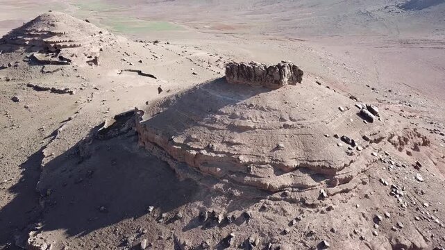 Aerial drone shot of a unique mountain summit in the High Atlas. Features natural geological caves used as ancient human shelters and a fortress-like rock formation in the Moroccan wilderness.