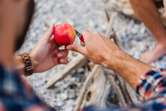 Person peeling apple with knife outdoors in summer nature setting