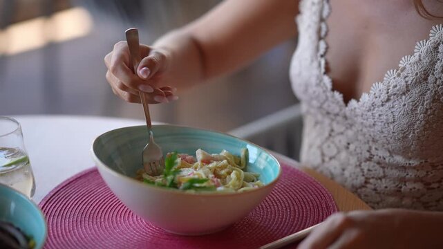Gastronomic Delight: A woman's gentle hand uses a fork to sample a delicious pasta dish, a vision of culinary refinement and taste.
