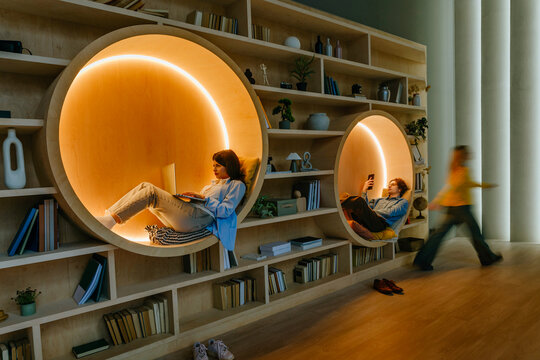 People relaxing with digital devices in cozy modern library coworking space