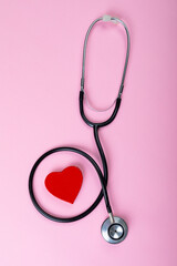 Overhead view of stethoscope around red heart shape on pink background with copy space © wavebreak3