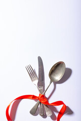 Overhead view of cutlery tied tightly with red ribbon below copy space over white background