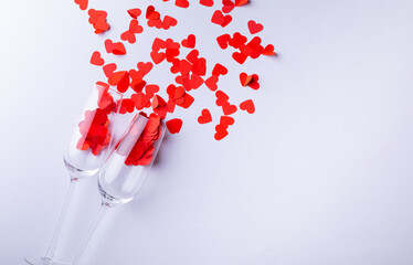 Champagne flutes with red heart shapes scattered by copy space over white background