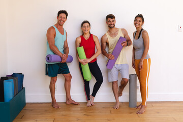 Fototapeta premium Portrait of smiling multiracial men and women with yoga mats against wall in yoga studio