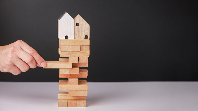 Hand careful removing wooden block from tower metaphor for risk control maintaining housing market balance in unstable economy with tension mood