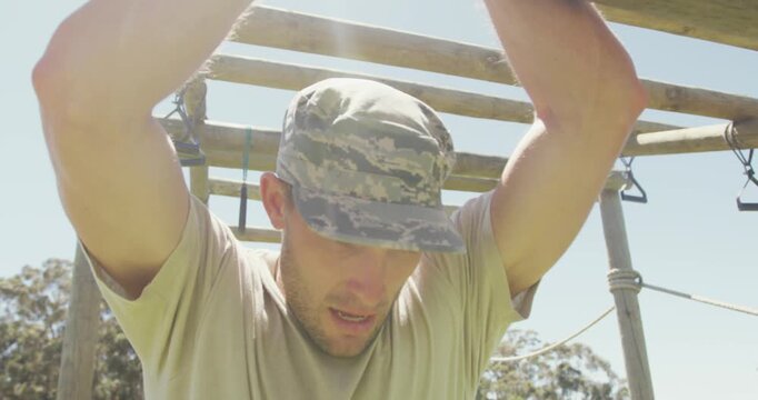 Tired caucasian male soldier hanging on monkey bars on army style obstacle course in the sun