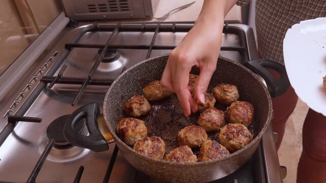 Hands carefully place the finished meatballs cutlets in the pan, the cook lays out even rows and adds the final leveling before serving, the stove and plate on the side create a practical atmosphere i