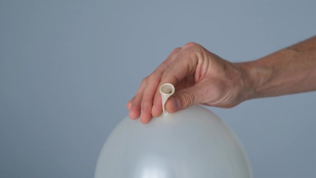 A man's hand holds a balloon and deflates it.
