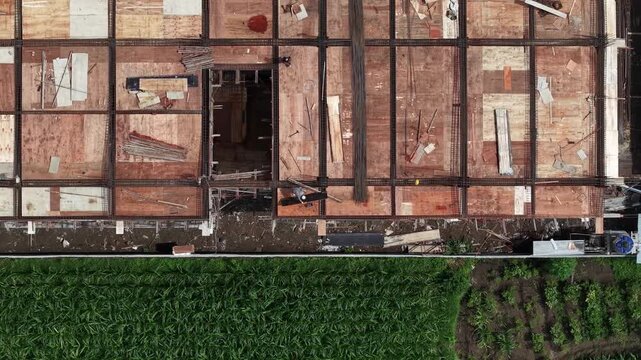 Aerial view of a construction site with wooden planks and metal frames next to a field of green grass, Klaten Regency, Central Java, Indonesia.