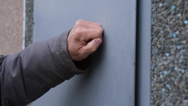 A man's hand knocks on a metal gate with his fist