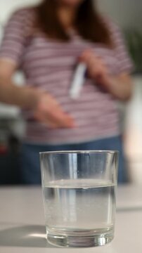 A person prepares vitamins and effervescent medications in a kitchen. They pour water into a glass and add the effervescent tablet. Bubbles form as it dissolves in the water.