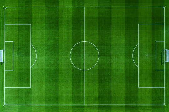 High-angle aerial top view of a pristine green soccer field. Professional football pitch with white markings, goal posts, and textured grass stripes. Perfect for sports and recreation designs.