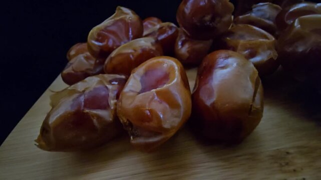 A high-quality, close-up shot of premium Saudi Khalas dates with a glossy golden-brown texture and thin skin, elegantly arranged on a rustic wooden board against a moody dark background, highlighting 