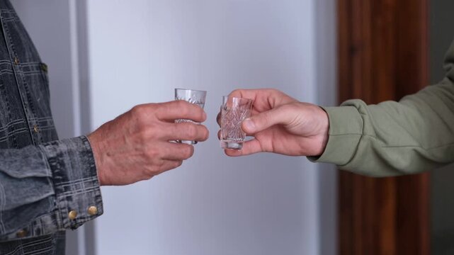 Two men's hands clinking glasses of vodka. Alcohol addiction.