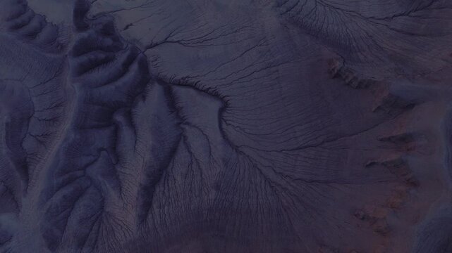 Aerial view of terrain reveals a network of stream-like patterns etched into the landscape, creating a striking contrast of dark and light tones, Hanksville, Utah, United States.