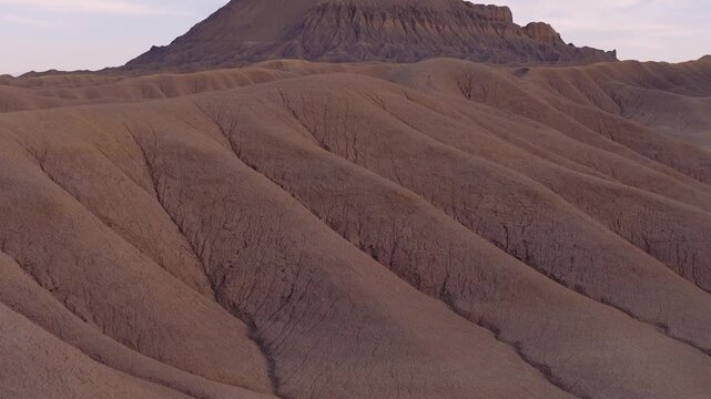 Aerial view of a rugged desert landscape with layered hills and a prominent mesa under a soft sky, creating a textured, earthy panorama, Hanksville, Utah, United States.