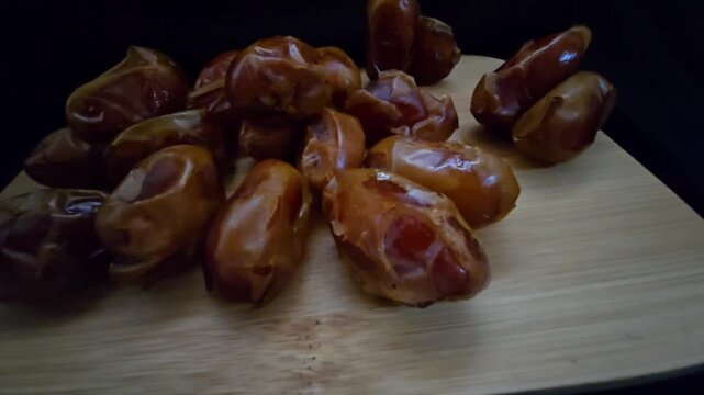 A high-quality, close-up shot of premium Saudi Khalas dates with a glossy golden-brown texture and thin skin, elegantly arranged on a rustic wooden board against a moody dark background, highlighting 