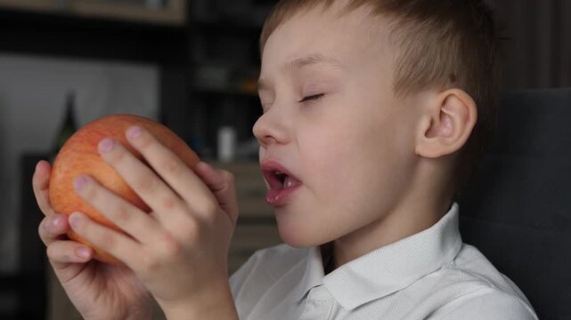 Cute boy eating a fresh red apple at home. Healthy snack and natural nutrition concept. 