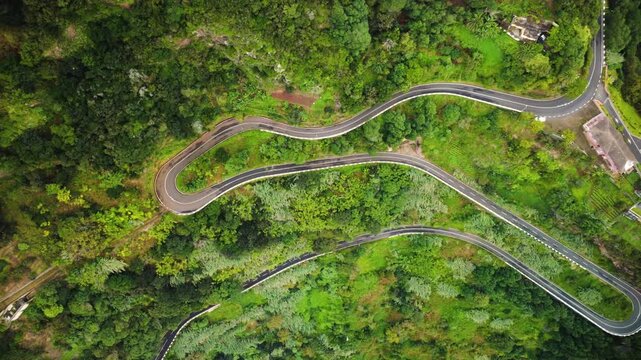 Aerial top down view of a car driving on a winding serpentine mountain road near Lombo do Pico, drone tracking sideways over hairpin bend and lush green terraces in Madeira island road trip