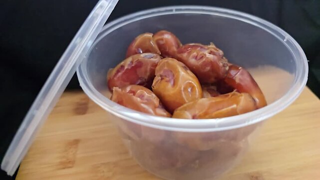 A close-up shot of premium Saudi Khalas dates packed in a transparent plastic round container, showcasing the soft texture and golden-brown color of the fruit. The video features a clear view of the d